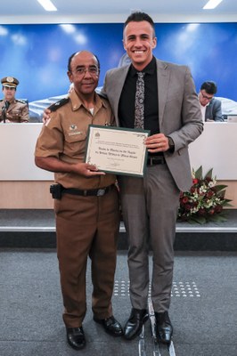 Presidente da Câmara Municipal, Ver. Douglas Dofu, entrega um agradecimento ao Ten. Wellington, maestro da Banda da PMMG.